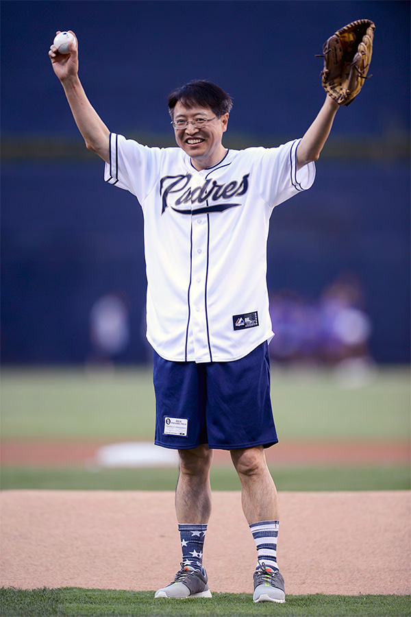 Sam Shen wearing Padres jersey with baseball and glove standing at pitcher's mound in stadium.